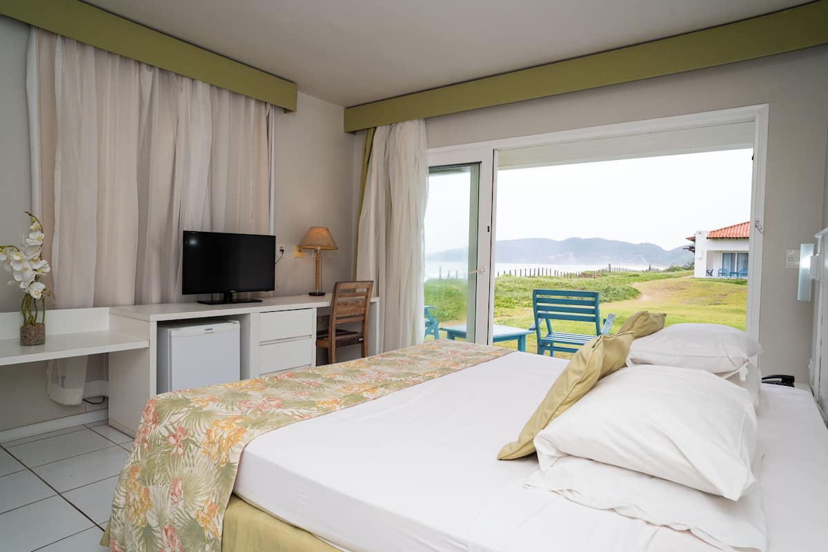 A hotel room with a bed, a desk with a television, a small fridge, and a view of the outdoors.