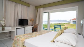 A hotel room with a bed, a desk with a television, a small fridge, and a view of the outdoors.