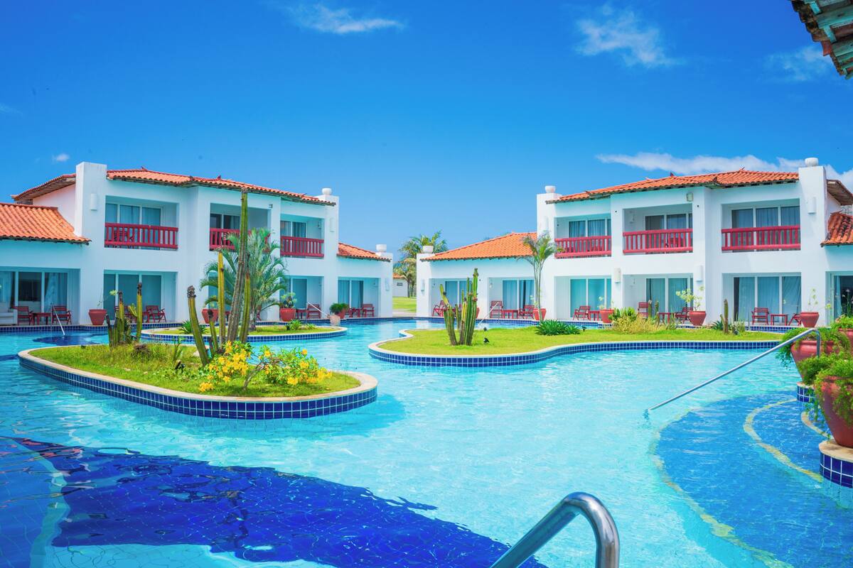 A hotel with a swimming pool, red balconies, and white walls.