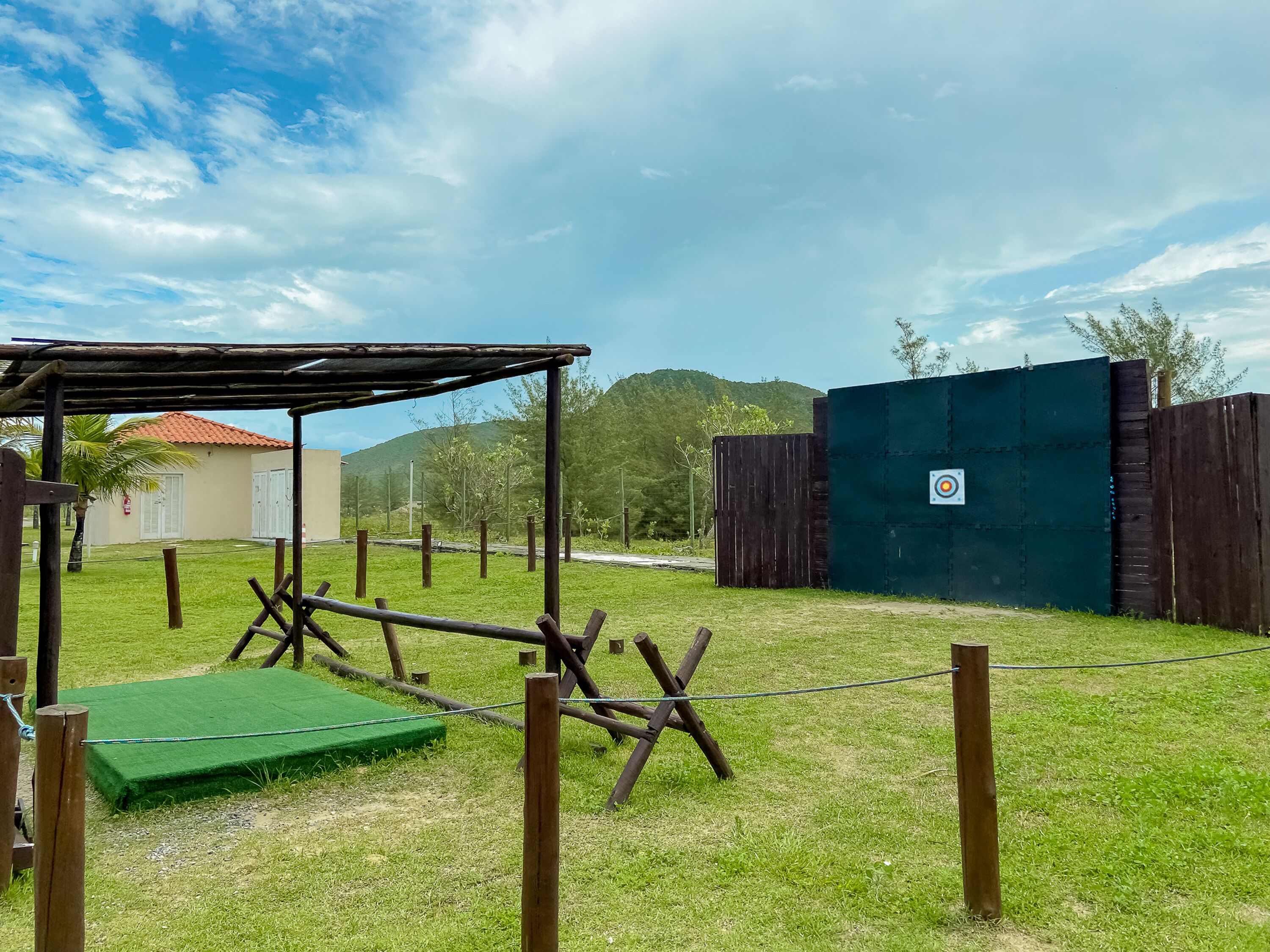 An outdoor area with a wooden structure, a green mat, and a fenced area with a target on the wall.