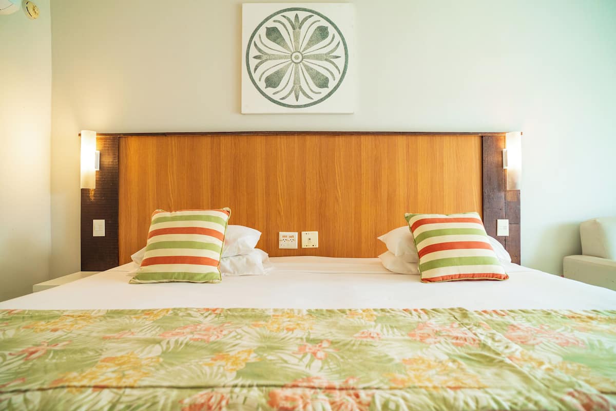 A hotel room with a wooden headboard, two pillows with striped patterns, a floral bedspread, and a decorative wall piece above the headboard.