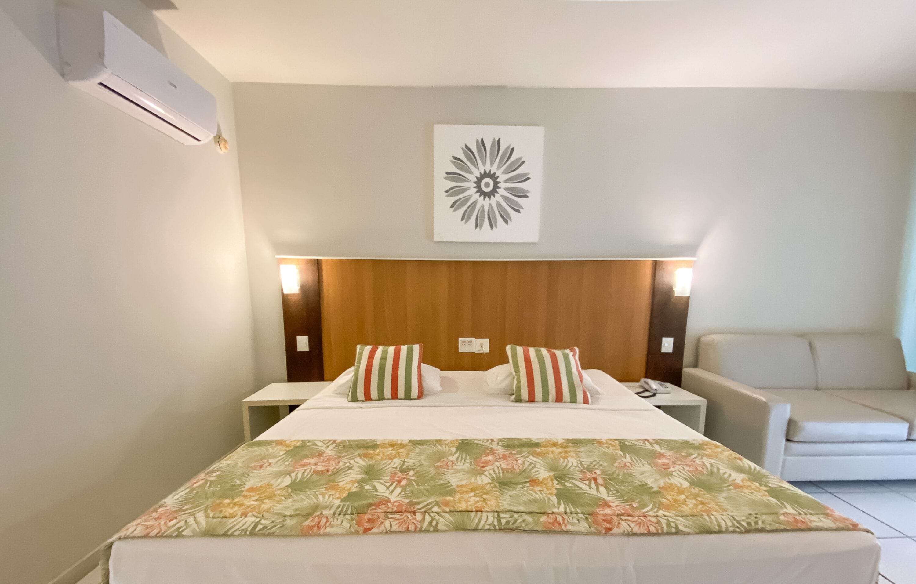Habitación de hotel con cama, mesita de noche, aire acondicionado instalado en la pared y una obra de arte en la pared.
