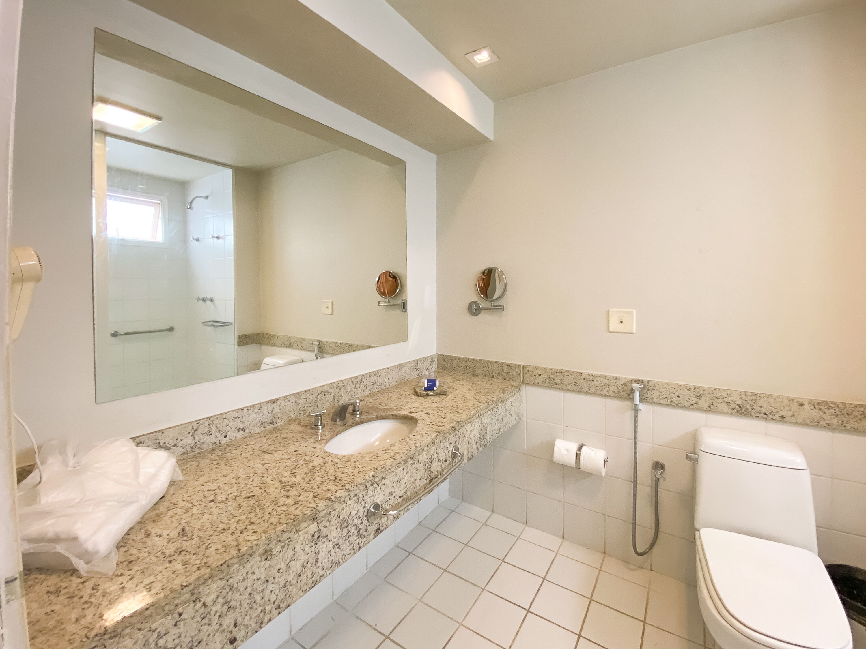A bathroom with a large mirror, a sink, a toilet, and a shower.