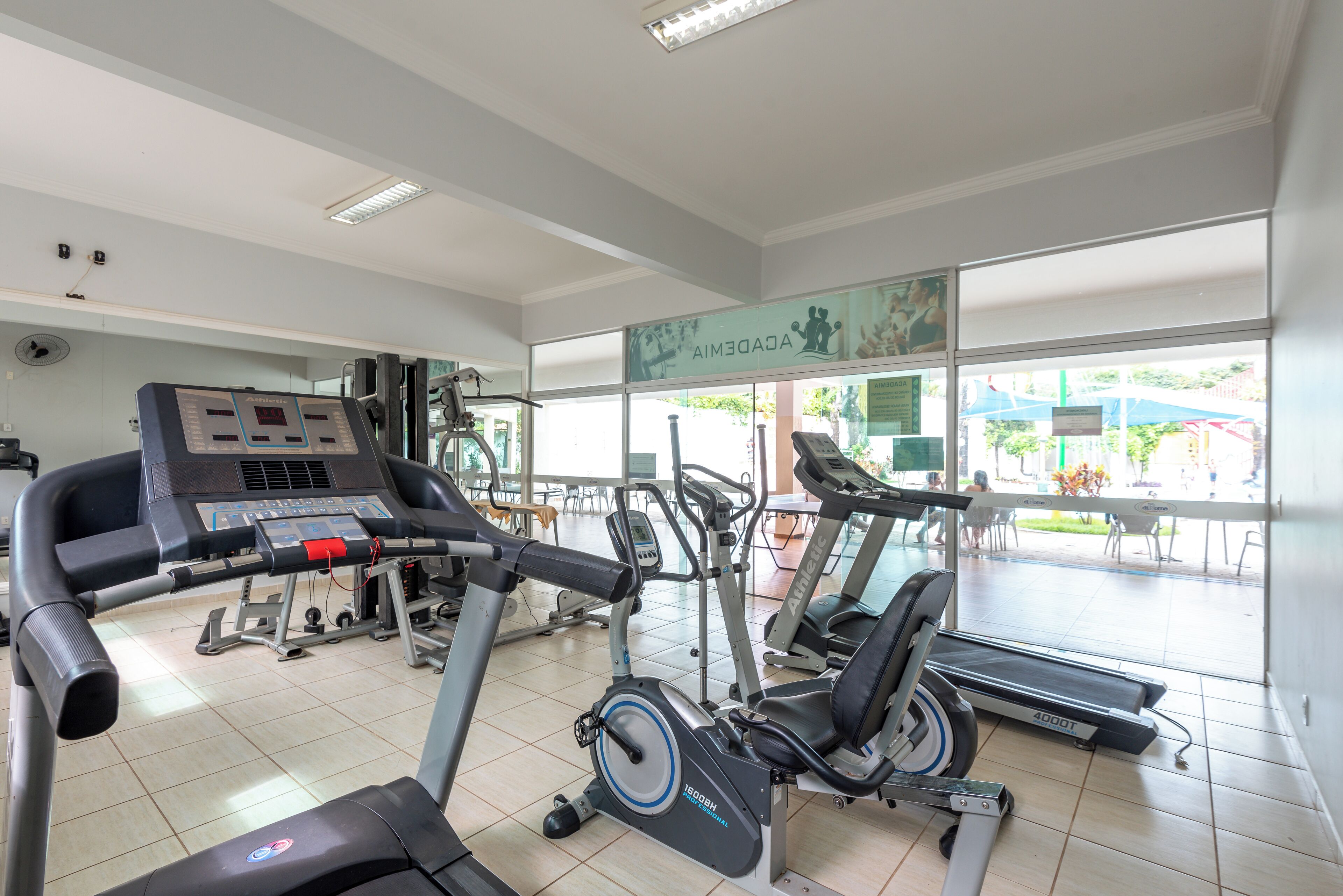 A gym with various exercise equipment, including treadmills and stationary bikes, and a large window providing a view of the outdoor area.