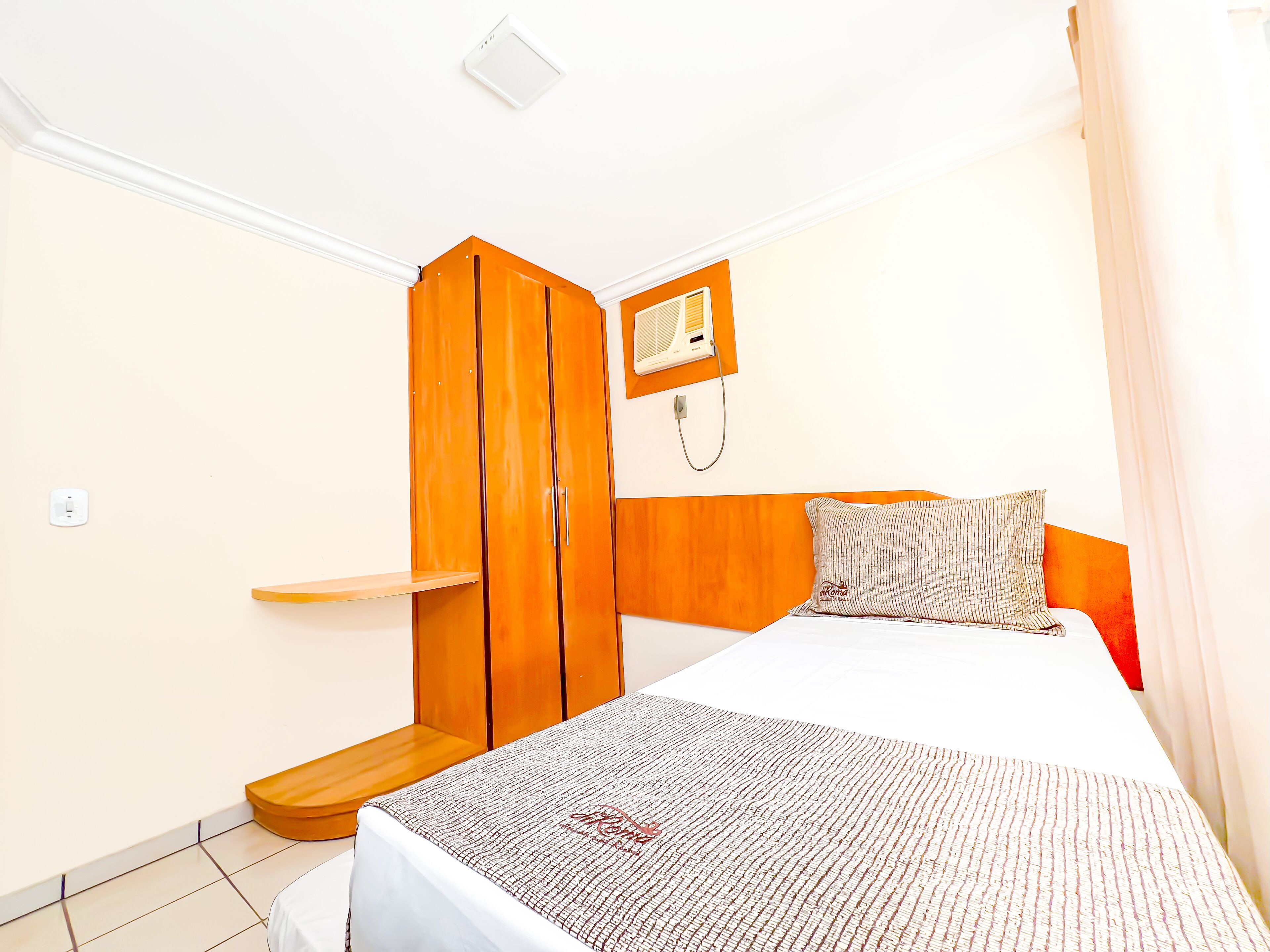 A bedroom with a bed, a wooden wardrobe, a bedside table, and a wall-mounted heater.