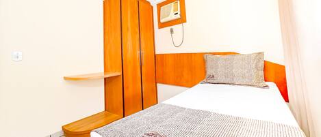 A bedroom with a bed, a wooden wardrobe, a bedside table, and a wall-mounted heater.