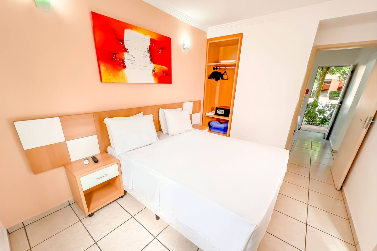A modern hotel room with a large bed, a nightstand, a wardrobe, and a painting on the wall.