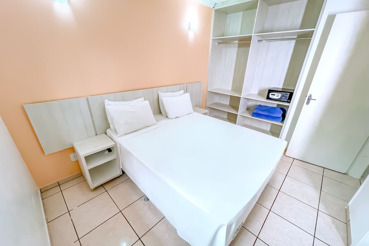 A neatly arranged bedroom with a bed, bedside tables, a wardrobe, and a small desk with a computer.