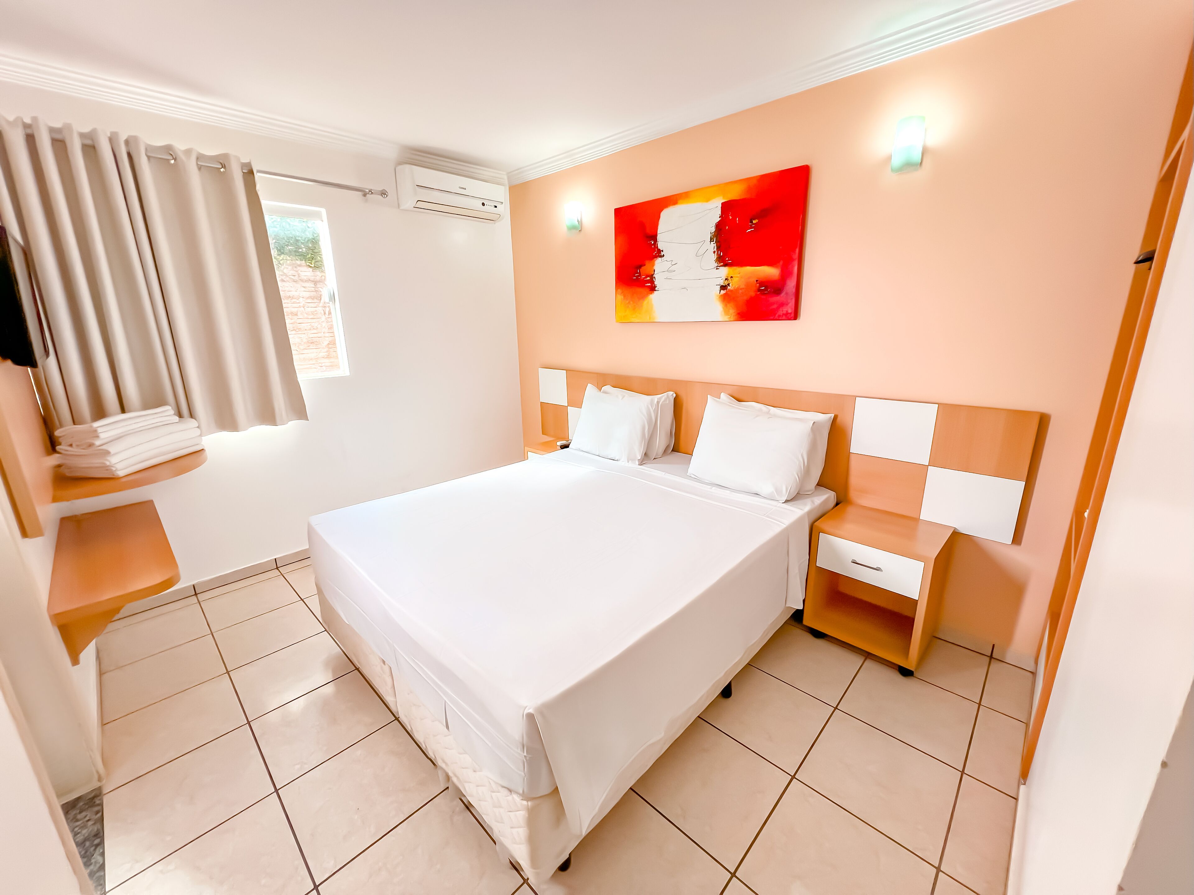 A modern hotel room with a large bed, a bedside table, a nightstand, and a wall-mounted air conditioner.