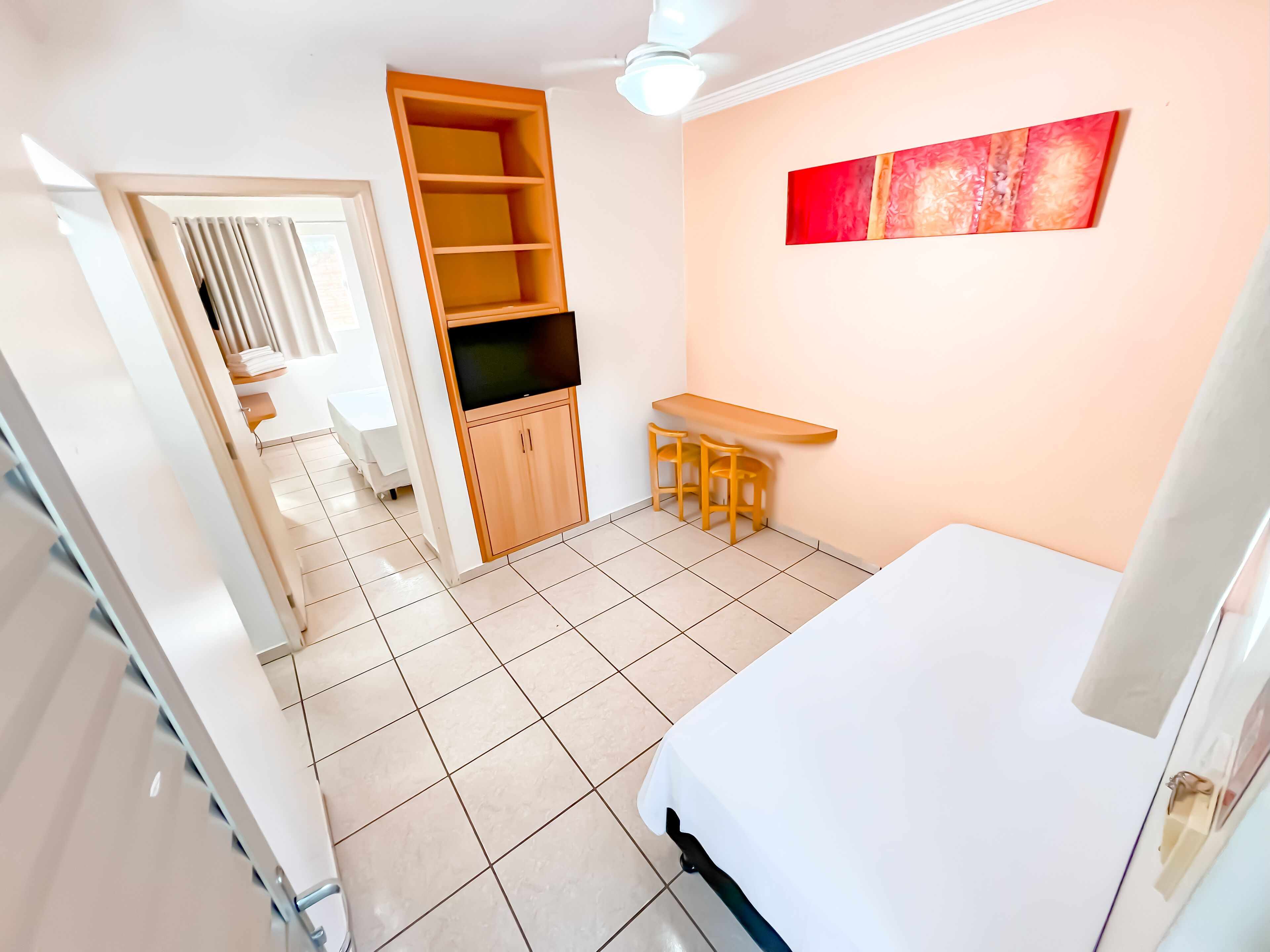 A room with a bed, a desk with two chairs, a wardrobe, and a ceiling fan.