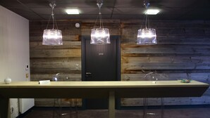 Un mostrador de recepción con tres lámparas colgantes, una pared de madera y una puerta con la etiqueta "privé".