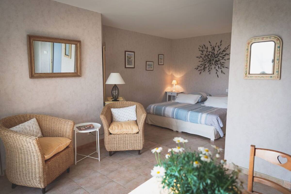 Une pièce comprenant un lit, deux fauteuils en osier, une petite table et un miroir fixé au mur.