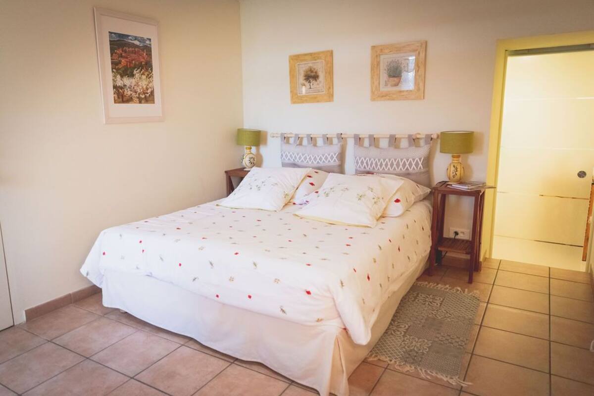 Une chambre à coucher avec un lit, deux tables de chevet, une porte et un mur orné de deux tableaux encadrés.