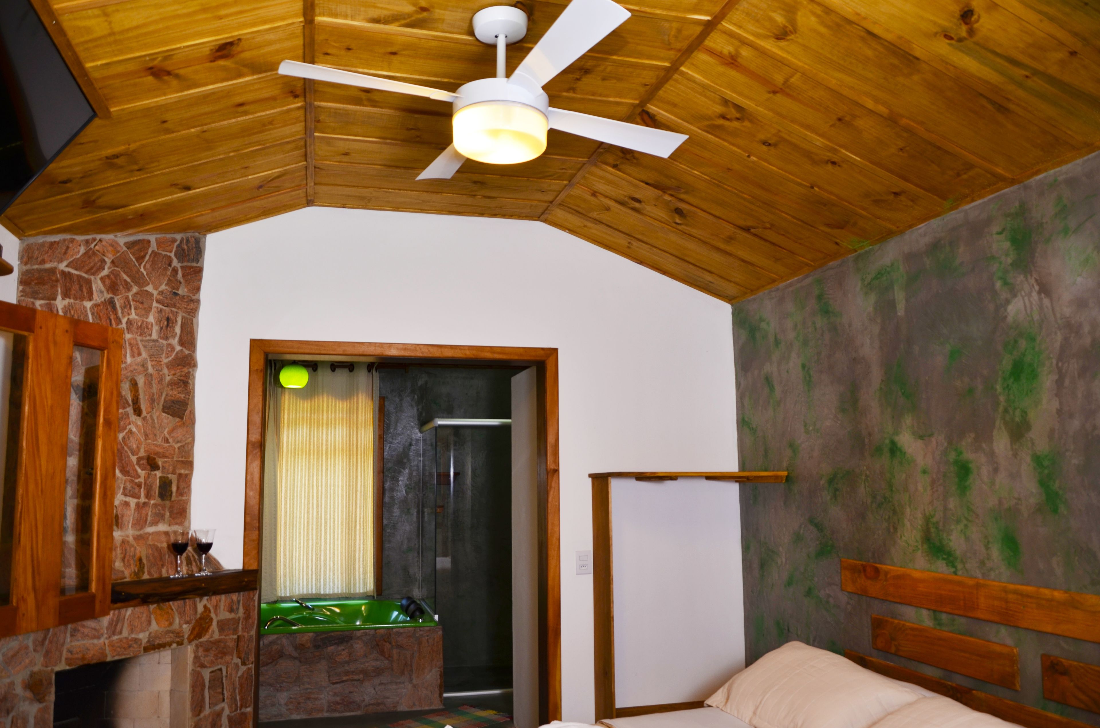 Une pièce dotée d’une cheminée en pierre, d’un ventilateur de plafond en bois et d’un lit avec une tête de lit en bois.