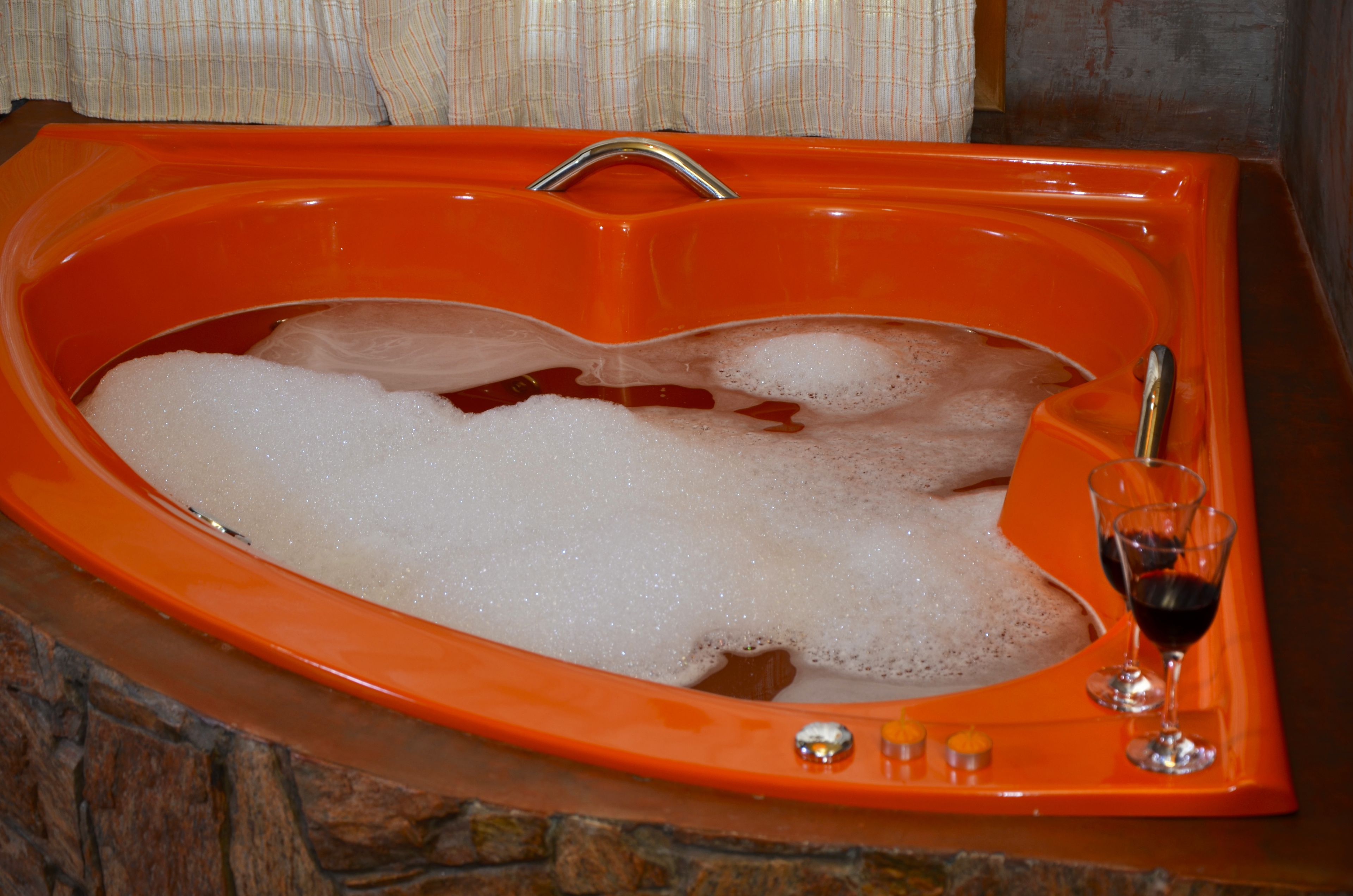 An orange bathtub filled with bubbles and a glass of red wine.