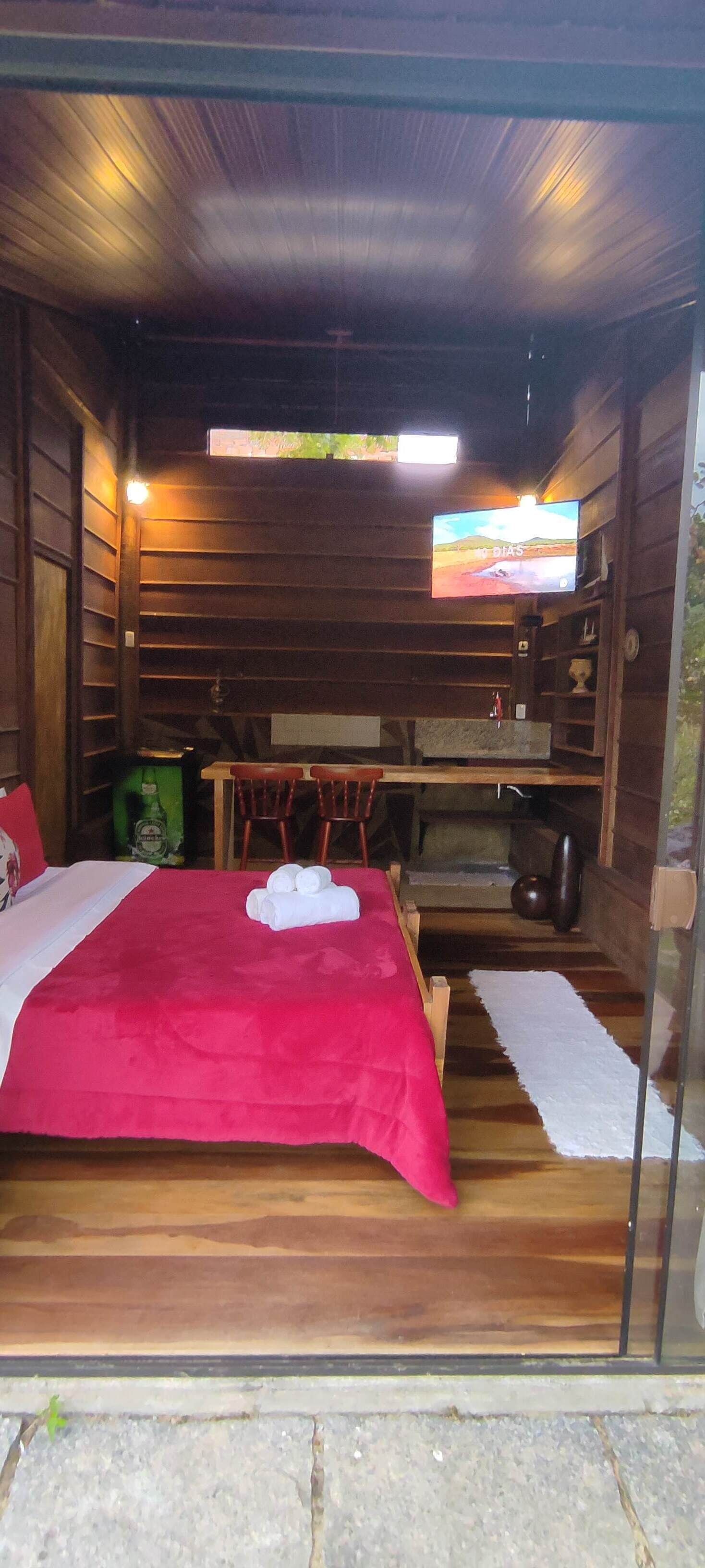 A wooden cabin room with a bed, a television, and a dining area.