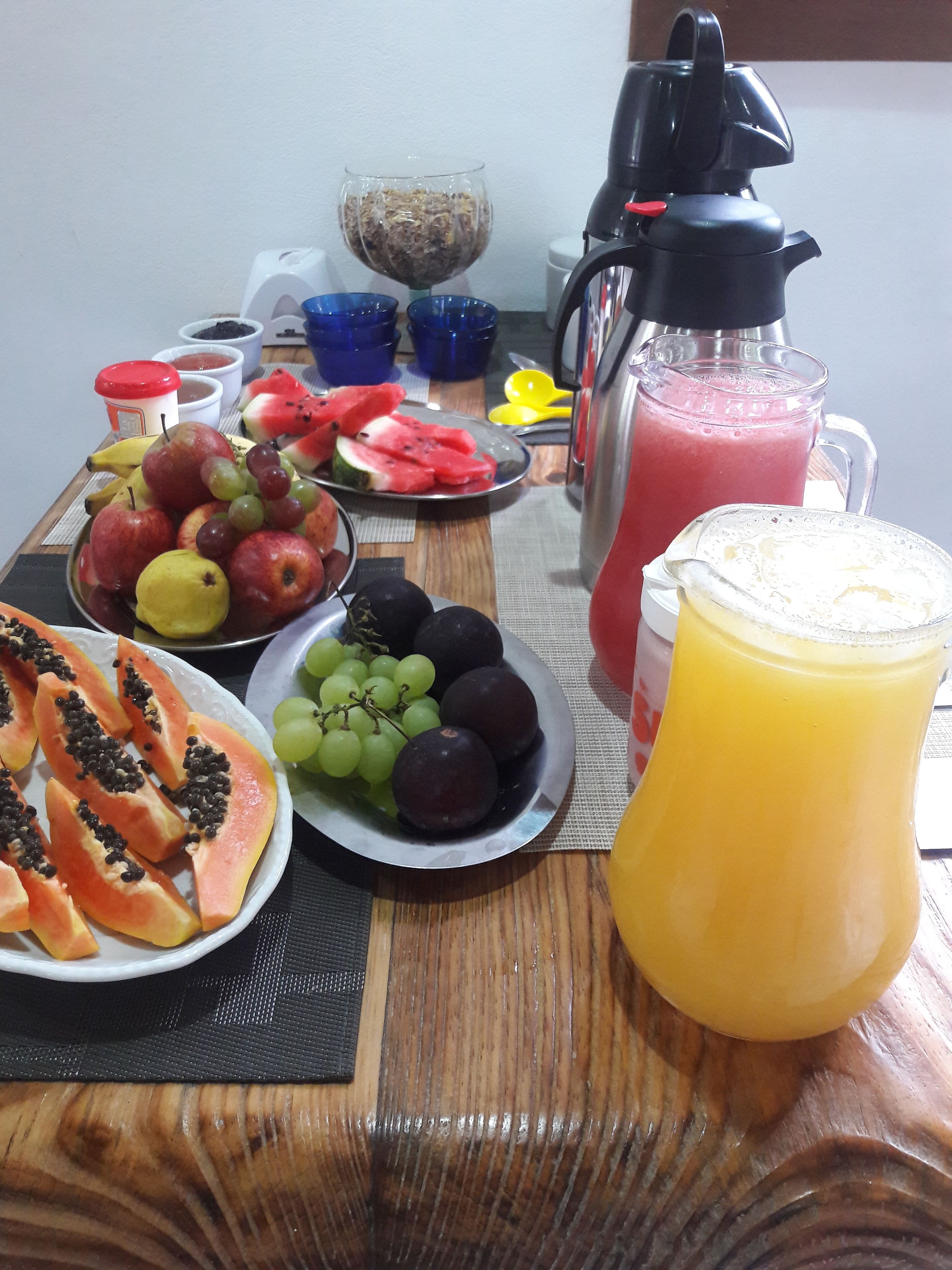 Una mesa de desayuno con frutas variadas, una licuadora y una jarra de jugo.