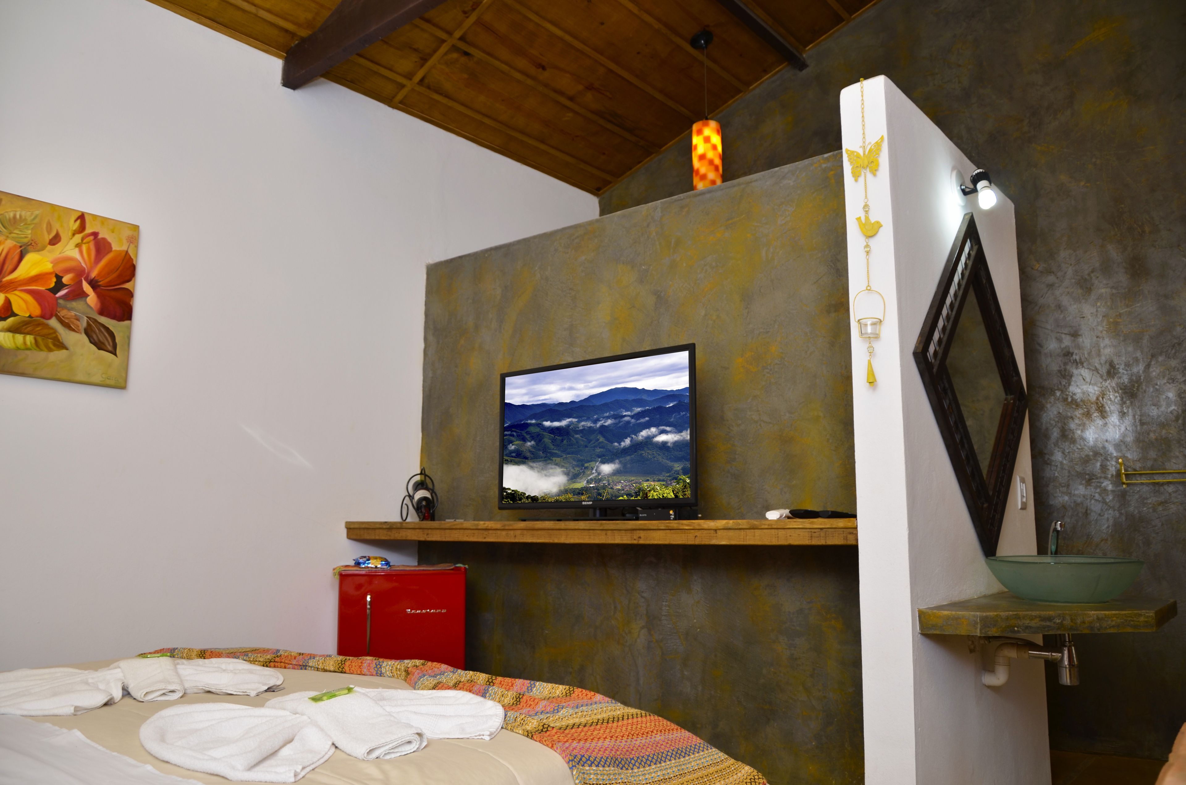 Un dormitorio con una cama, un televisor montado en una pared texturizada, un armario rojo y un lavamanos verde.