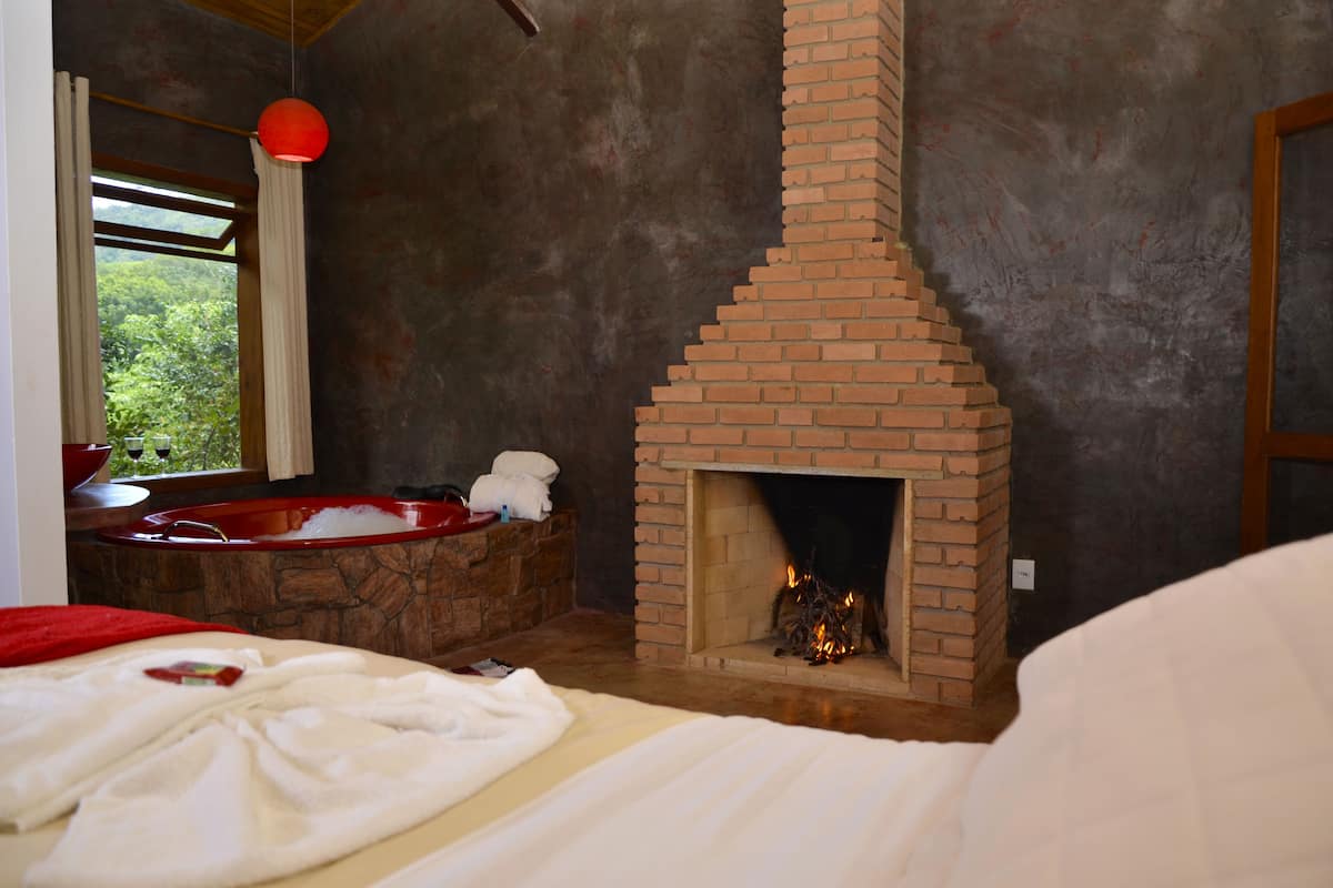 Un dormitori amb una llar de pedra, una finestra gran amb cortines i una banyera vermella.
