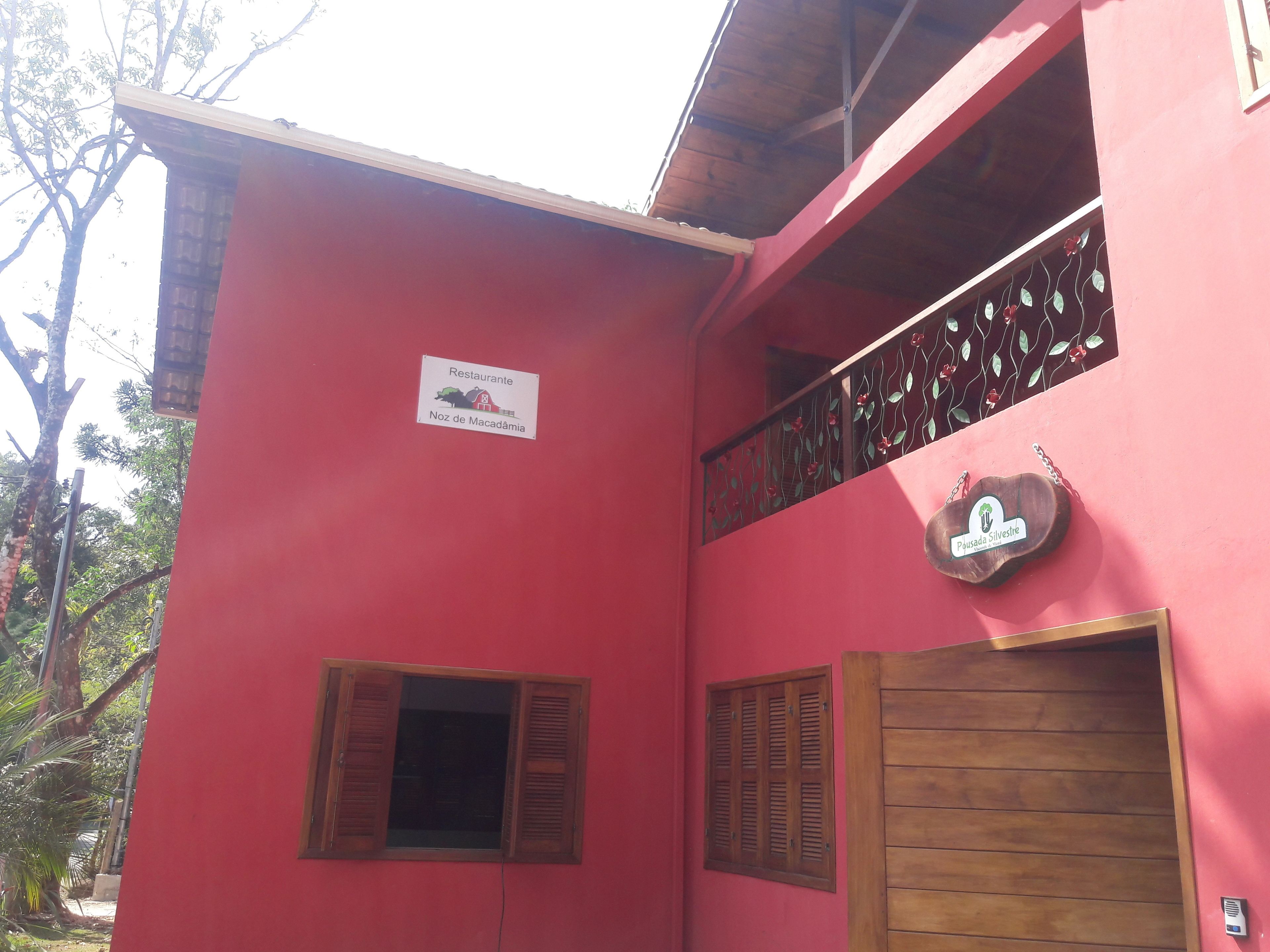 Un edificio rojo con un letrero que dice 'Noz de Macadamia', una puerta de madera y un balcón con barandas de metal.