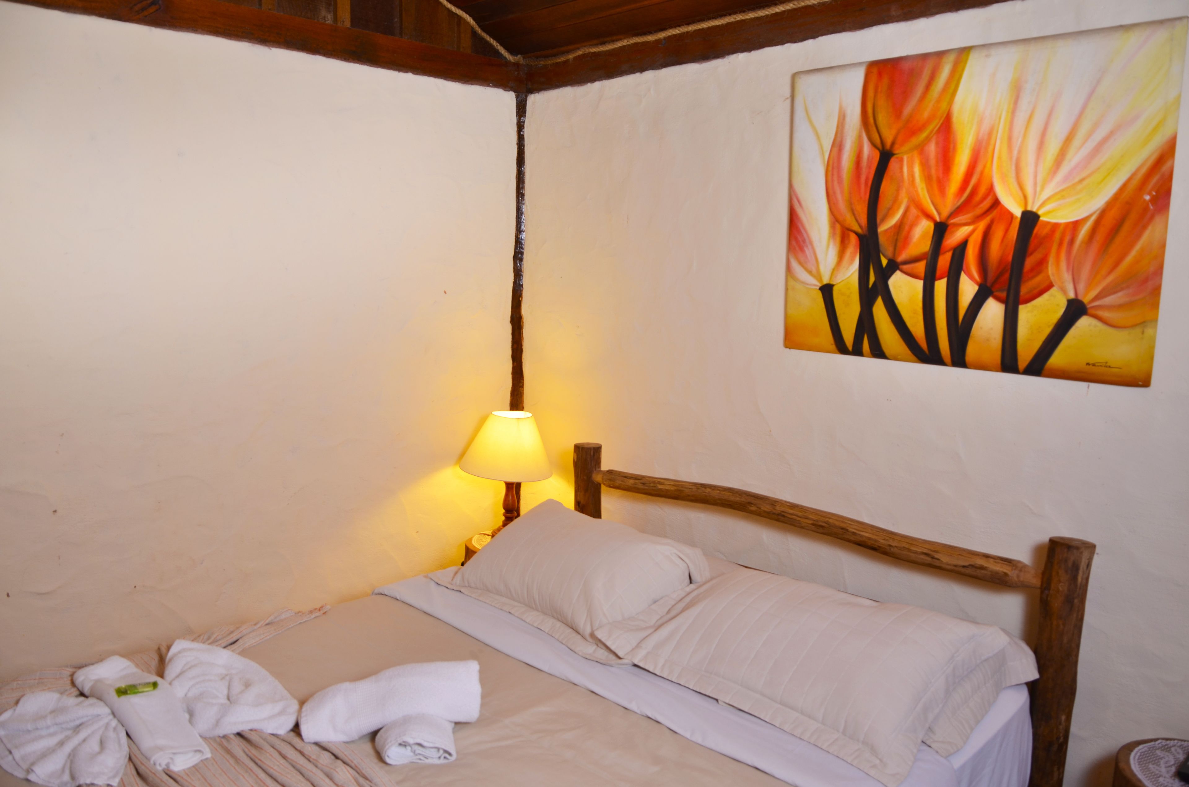 Una cama con cabecera de madera, una mesita de noche con lámpara y un cuadro de flores en la pared.