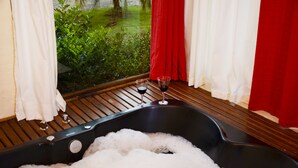 Eine Badewanne voller Blasen, ein Glas Rotwein und Blick auf Grün hinter einem Fenster.