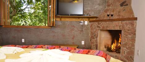 Un dormitorio con cama, televisión, chimenea y ventana con vistas a zonas verdes.