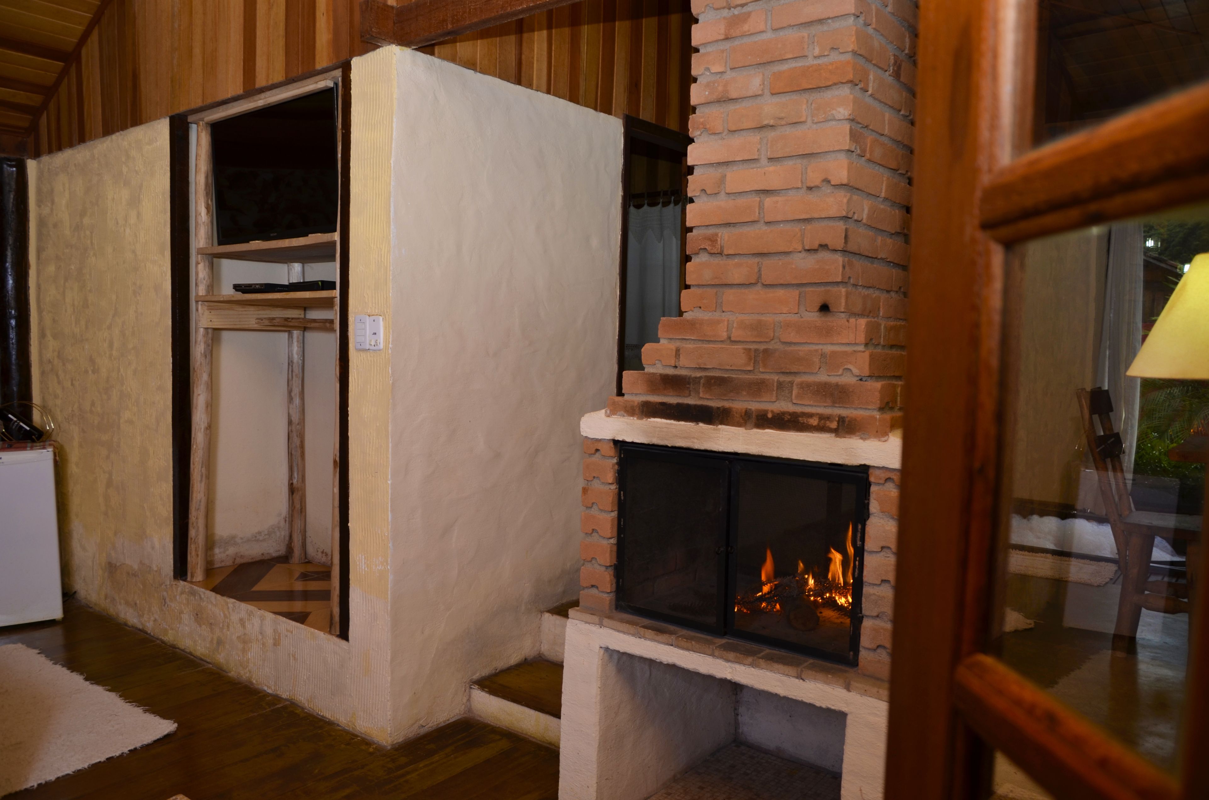 Una habitación con chimenea de ladrillo, vigas de madera en el techo y una pared blanca con ventana.