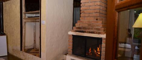 Una habitación con chimenea de ladrillo, vigas de madera en el techo y una pared blanca con ventana.