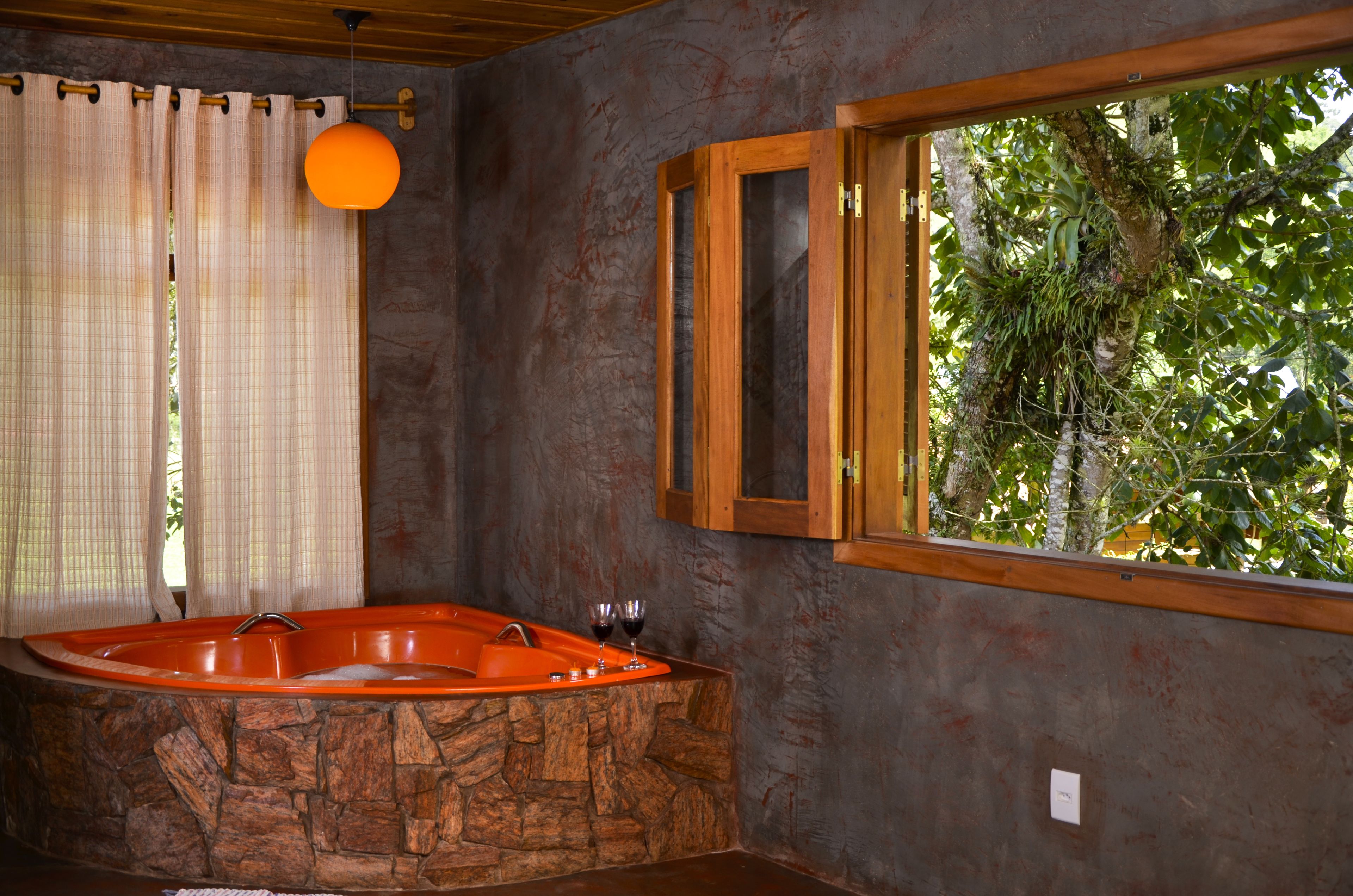 A bathroom with a stone bathtub, a wooden window frame, and a hanging orange light fixture.