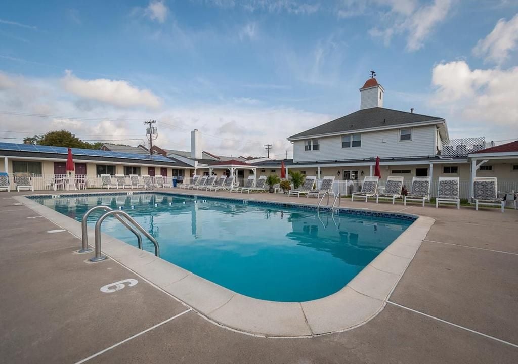 A swimming pool with lounge chairs and a building with a red roof.