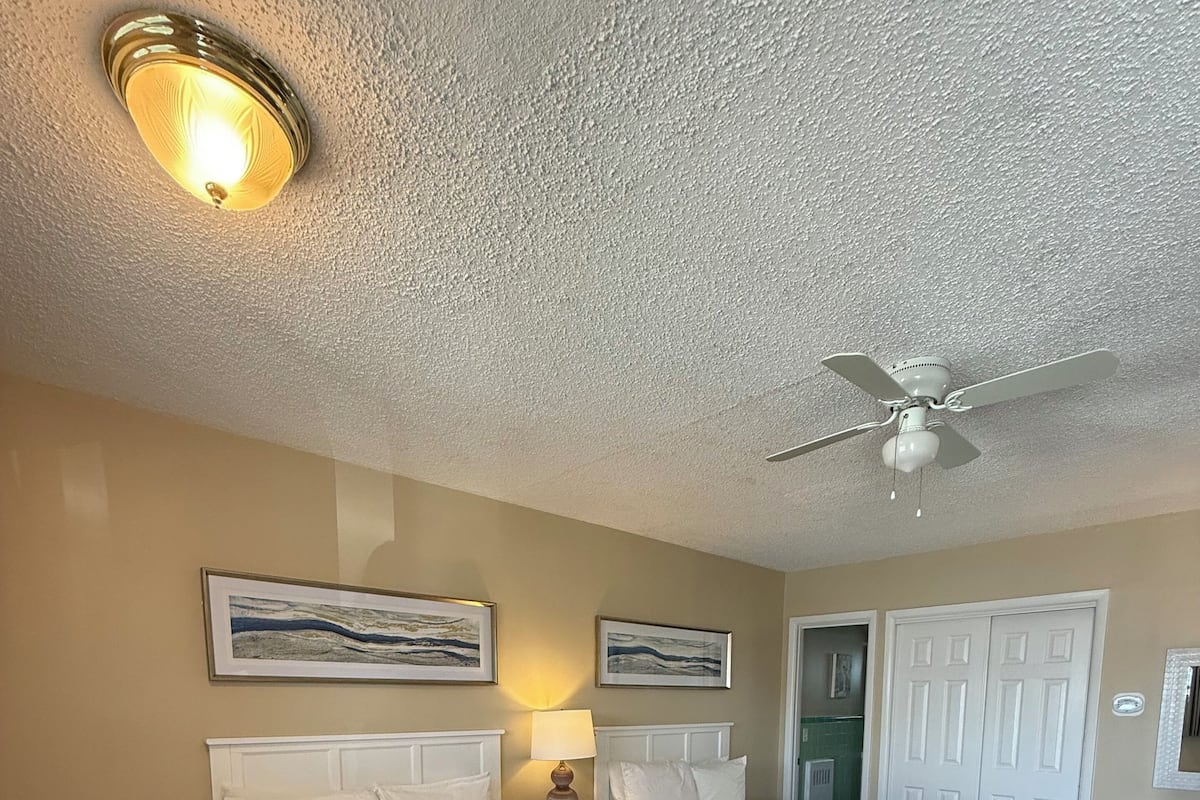 A hotel room with two beds, a ceiling fan, and artwork on the walls.