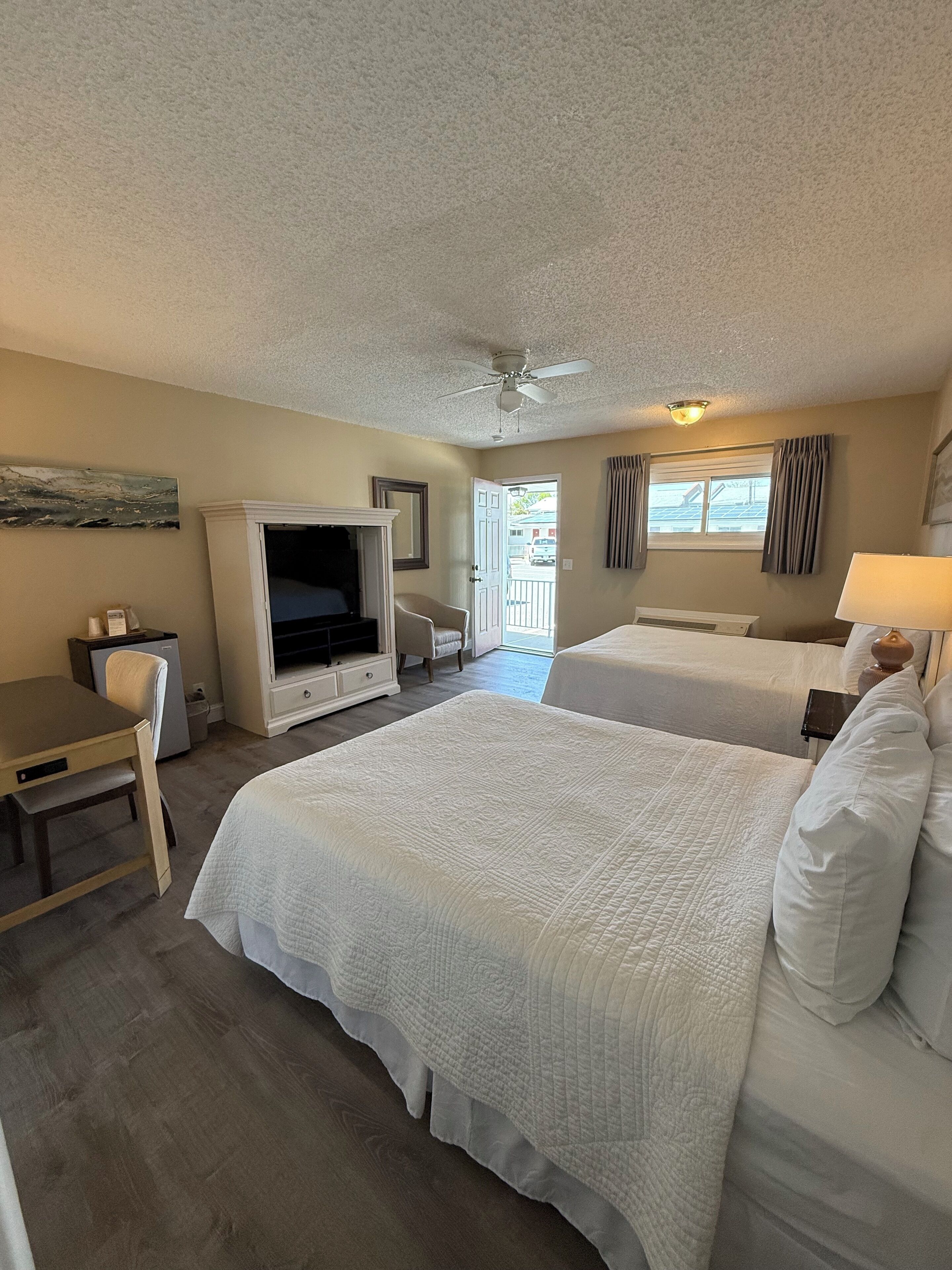 A hotel room with two beds, a desk, a television, and a ceiling fan.