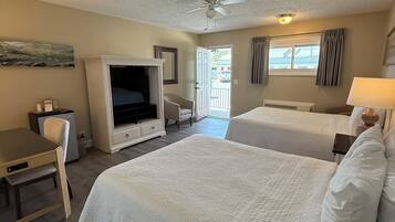 A hotel room with two beds, a desk, a television, and a ceiling fan.