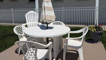 A patio with a round table and white chairs, a striped umbrella, and a potted plant with flowers.