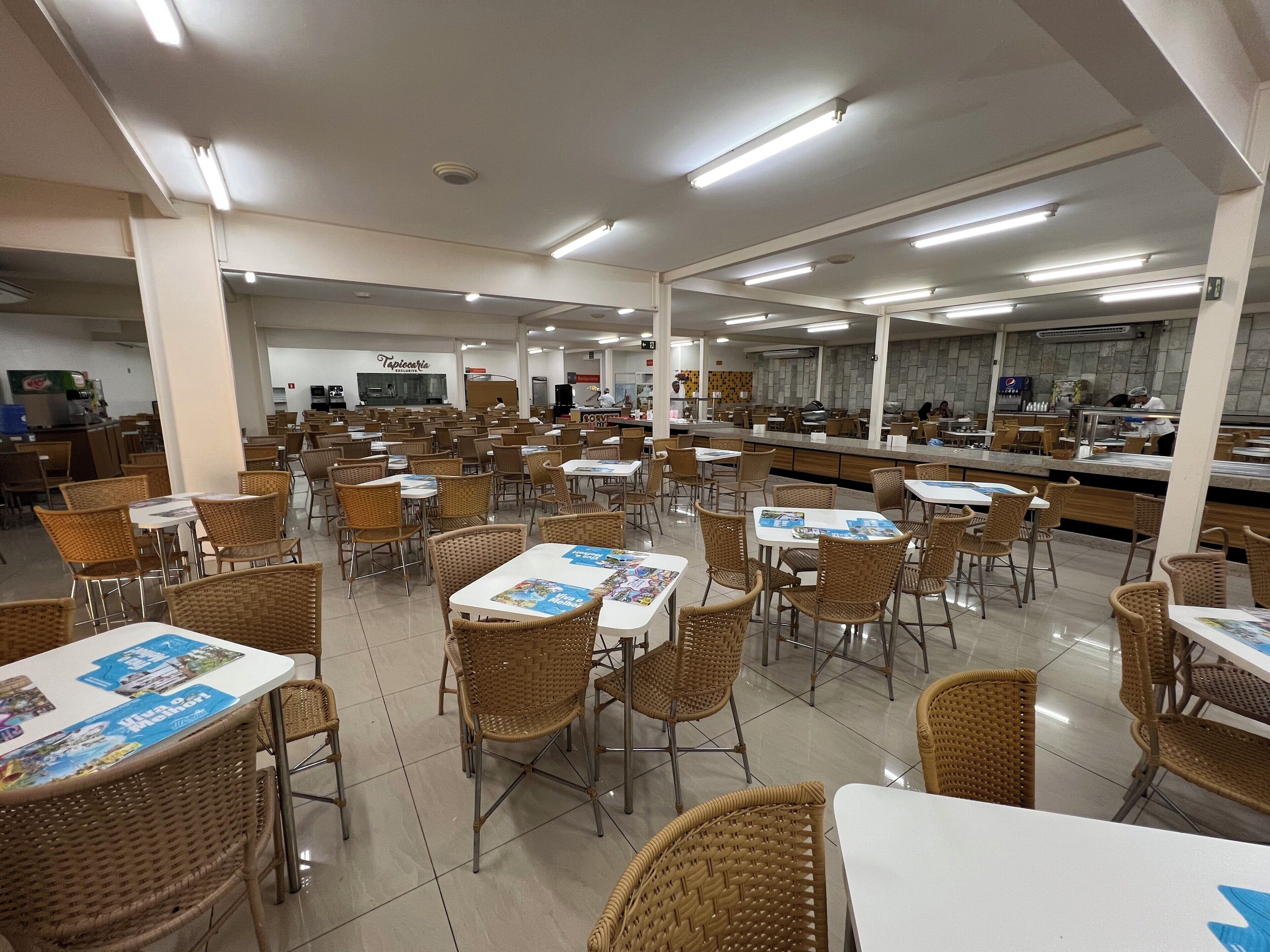Una amplia cafetería con varias mesas y sillas, un área de cocina y una zona de estar con vista a la cocina.