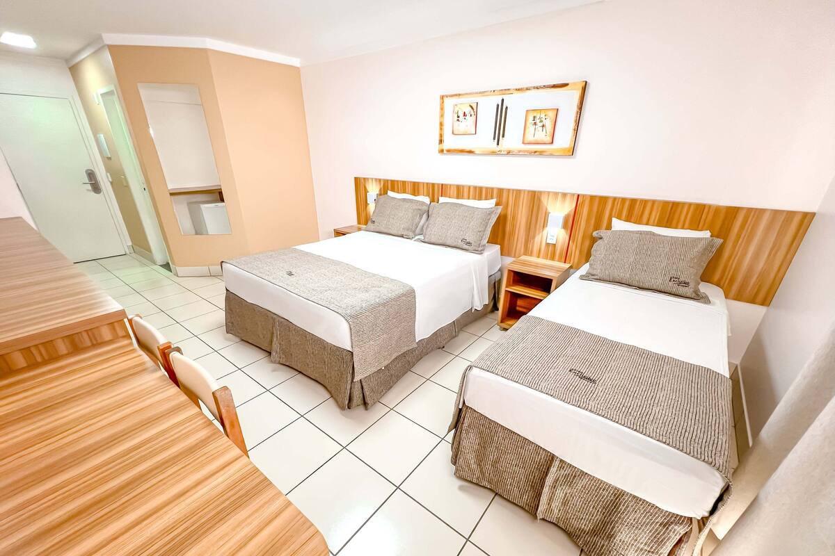 A hotel room with two beds, a wooden headboard, a small bedside table, and a wall-mounted picture.