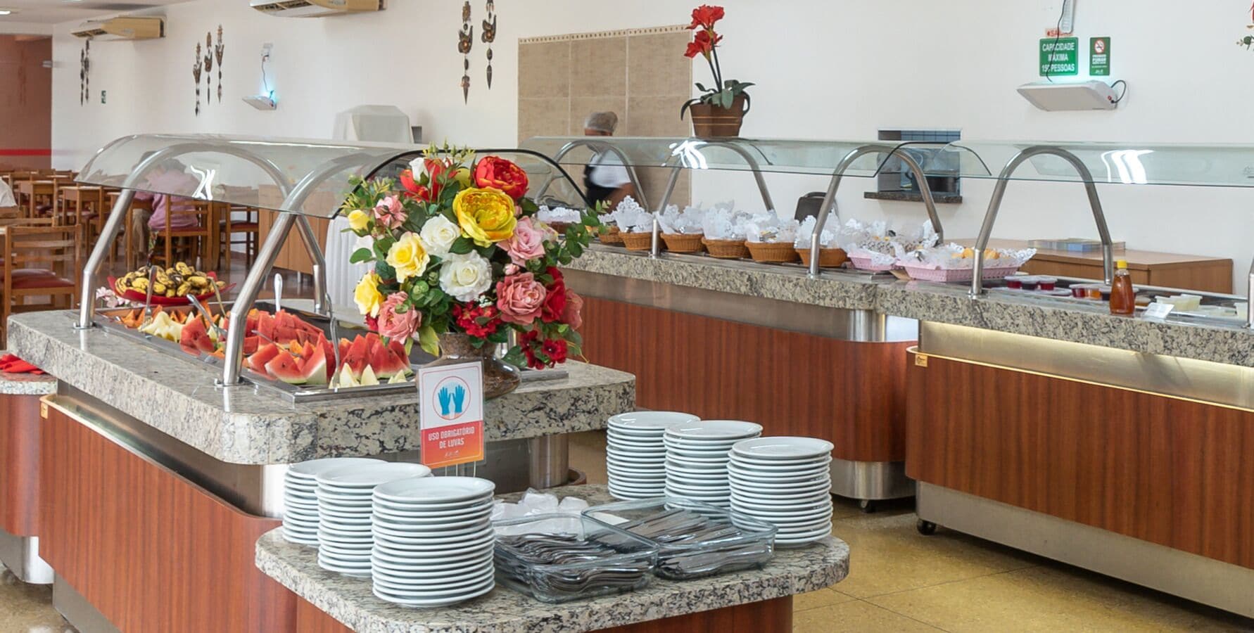 A buffet area with a variety of fruits, a floral centerpiece, and stacked plates.