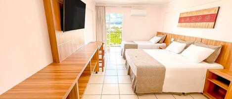 Une chambre d’hôtel avec un bureau en bois, deux lits simples, un grand lit, une télévision et un balcon avec vue.