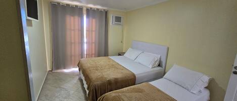 A hotel room with two beds, a window with curtains, a ceiling light, and a wall-mounted air conditioner.