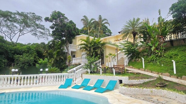 Una piscina con sillas de descanso azules, rodeada de follaje y una cerca blanca.