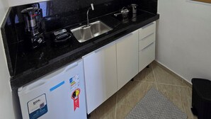 Una cocina compacta con encimera negra, armarios blancos, microondas integrado, un lavabo y un refrigerador pequeño.