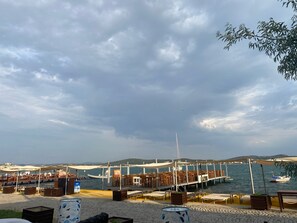 A waterfront restaurant with outdoor seating, a pier extending into the water, and boats nearby. - Cunda Deniz Hotel (Ayvalik)