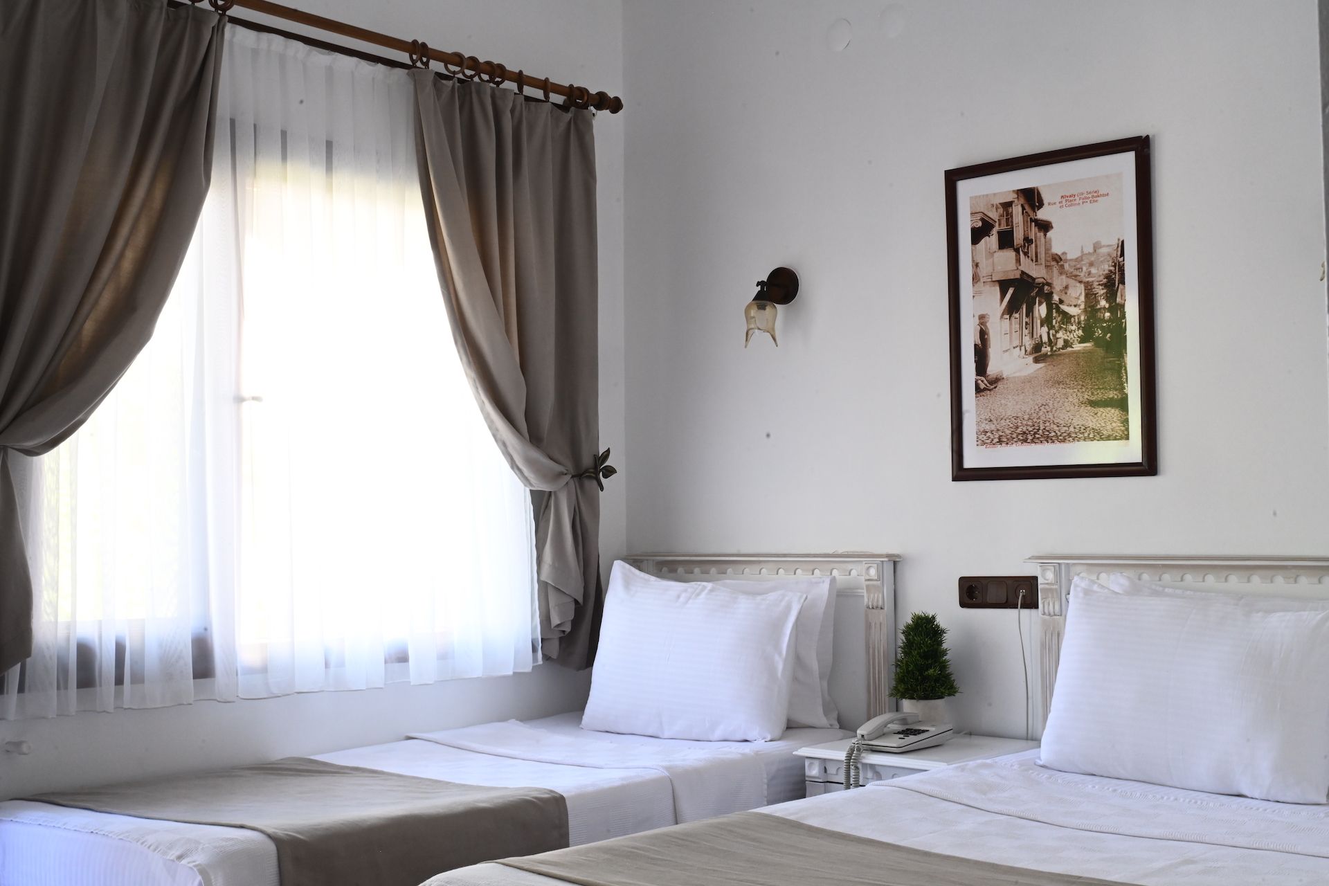 A hotel room with two beds, a window with curtains, a wall-mounted telephone, and a framed picture.