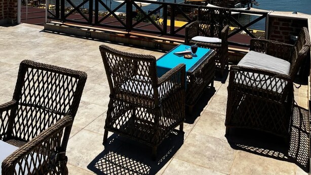 An outdoor seating area with wicker furniture, a pool table, and a view of boats on the water. - Cunda Deniz Hotel (Ayvalik)