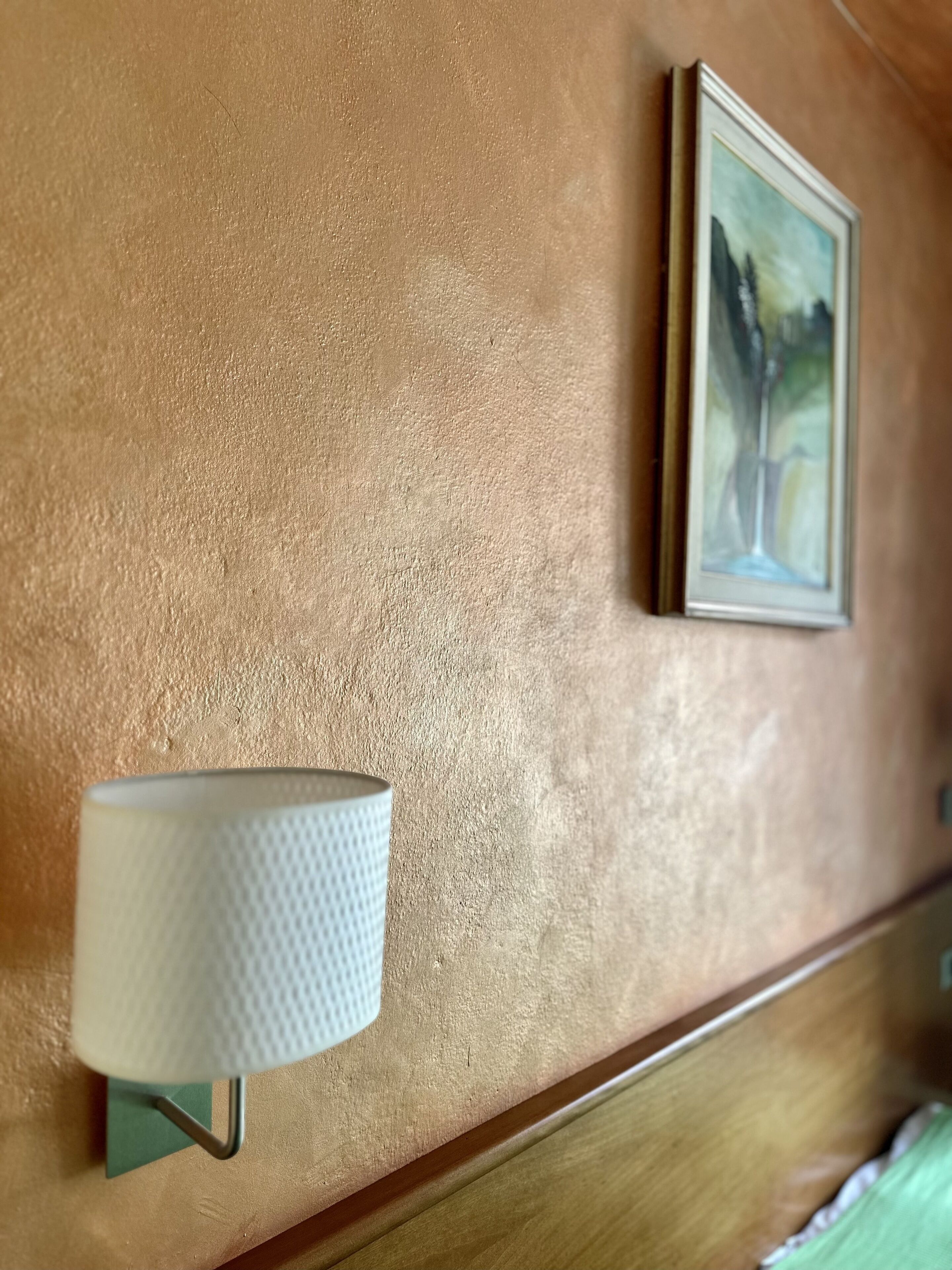 Un mur à texture, orné d’un tableau encadré et d’une lampe fixée au mur.
