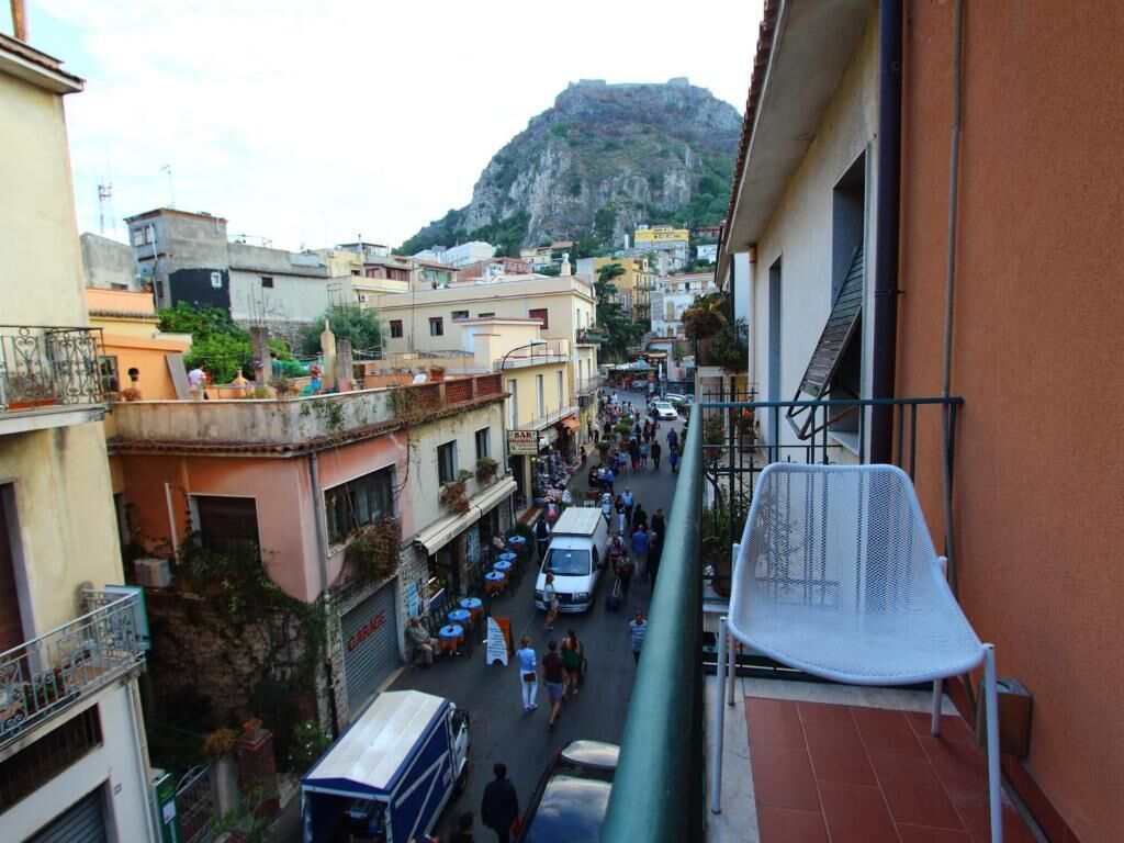 Una calle estrecha con edificios a ambos lados, una montaña al fondo y una silla blanca en el balcón.