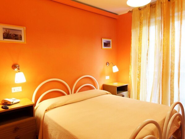 A hotel room with a bed, two bedside tables, two wall-mounted lamps, a nightstand, and a window with curtains. - Hotel Innpiero Taormina (Taormina)