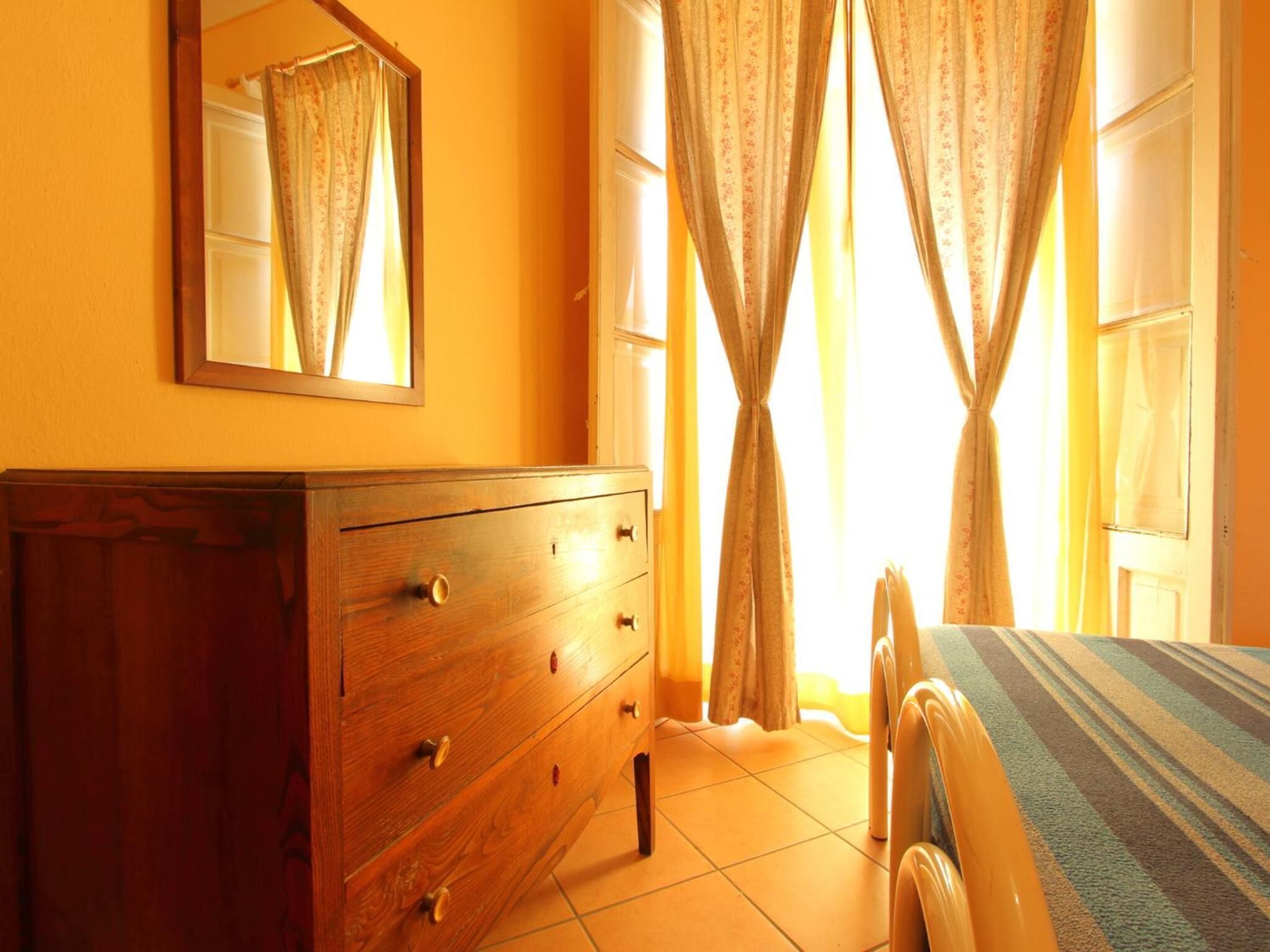A bedroom with a wooden dresser, a bed with a striped bedspread, and curtains on the windows.