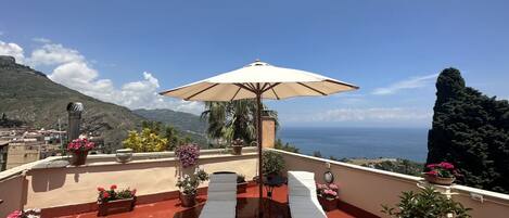 A rooftop terrace with two sun loungers, a table, and an umbrella.